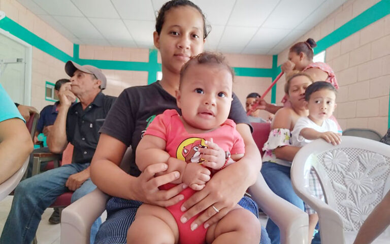 A woman holds a baby, with several people sitting around.